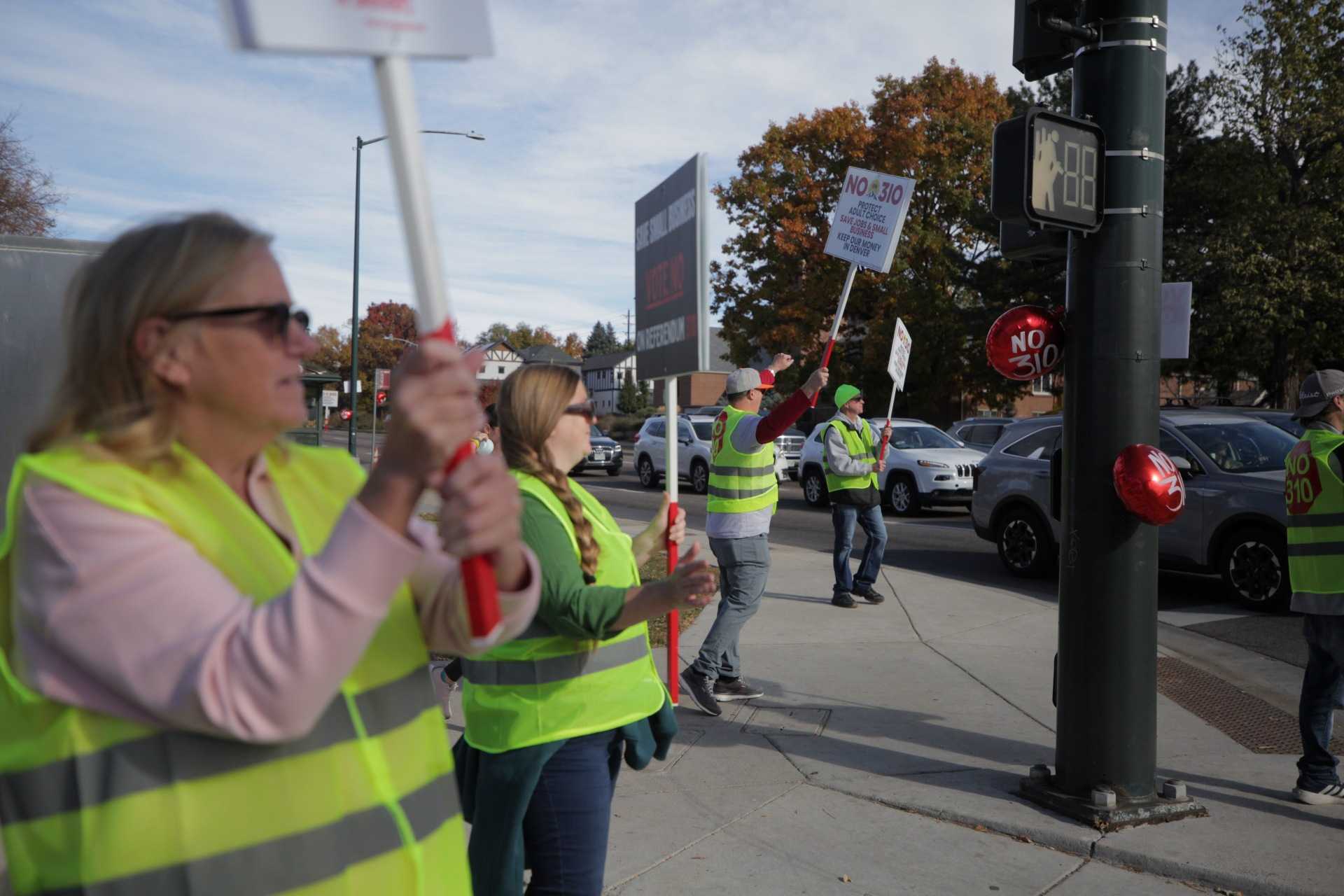 People in yellow safety vets hold &quot;No on 310&quot; signs on a busy street corner.