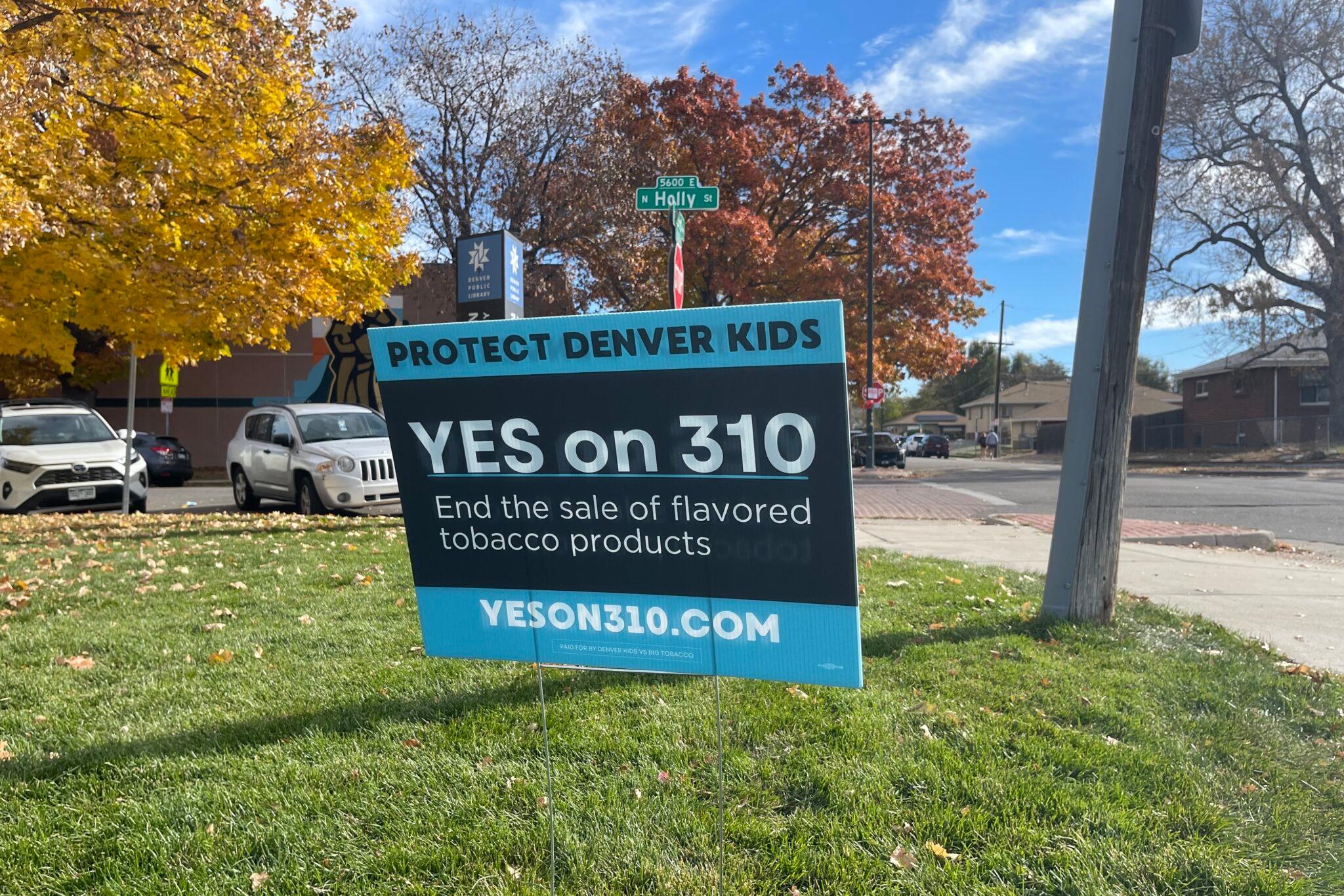 A &quot;Yes on 310&quot; sign is posted in a grassy area, with parked cars and tress with fall leaves.