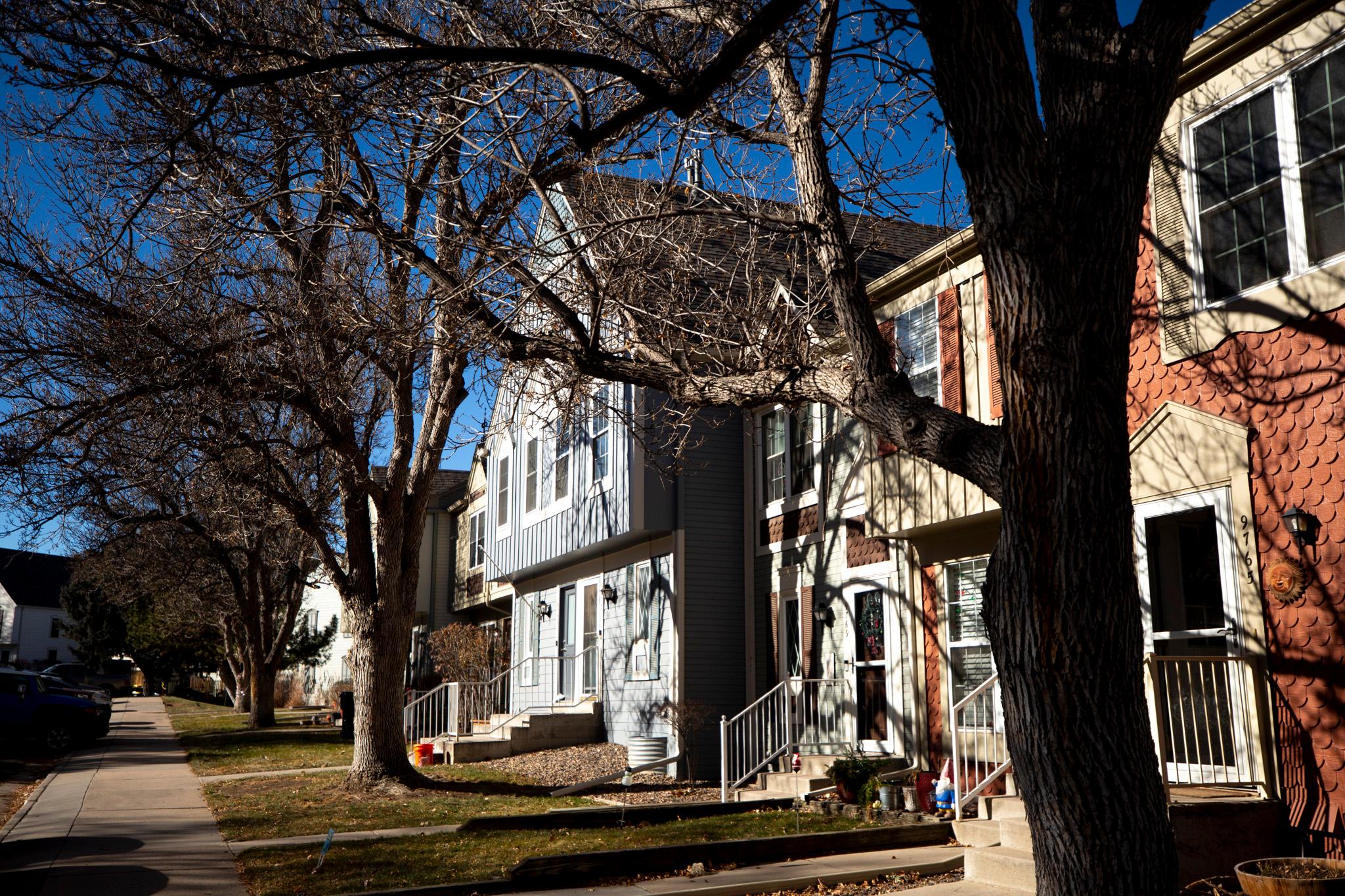 A row of townhomes, all different muted colors, on a suburban street.