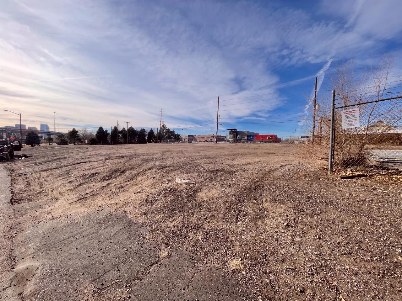 Brown dirt and a blue sky in an empty lot with a fence in the foreground.