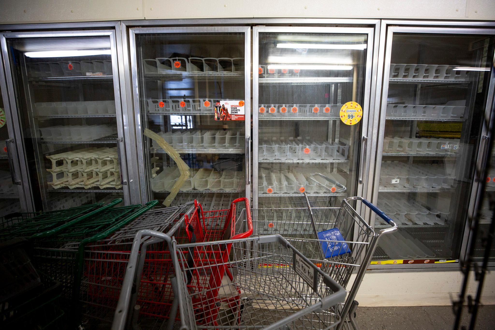An empty row of glass grocery freezer doors, with a row of carts stacked in front of it.