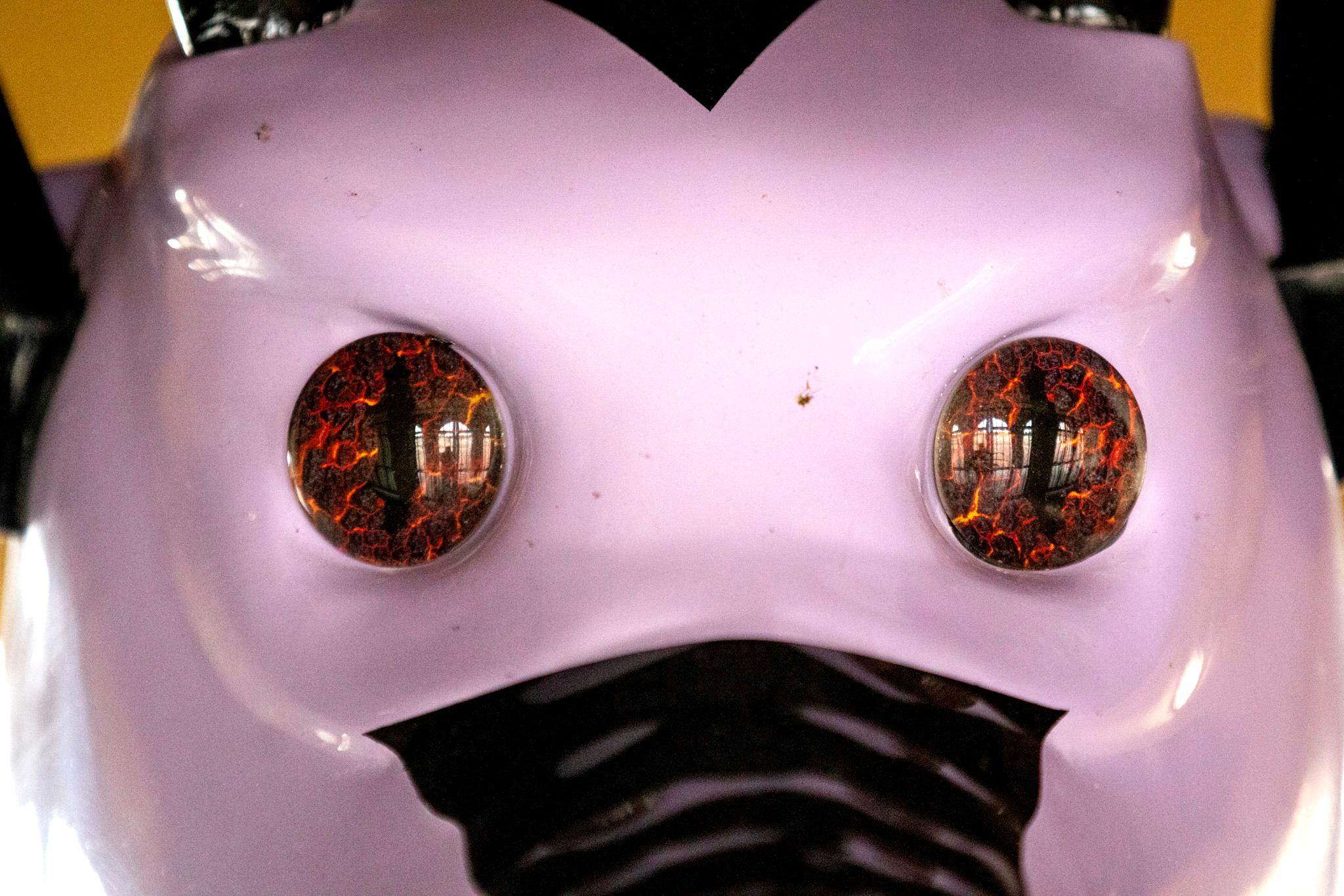 A close-up on the face of a purple dragon. Its eyes are dark with lines of red, like glowing magma, staring into the viewer's soul.