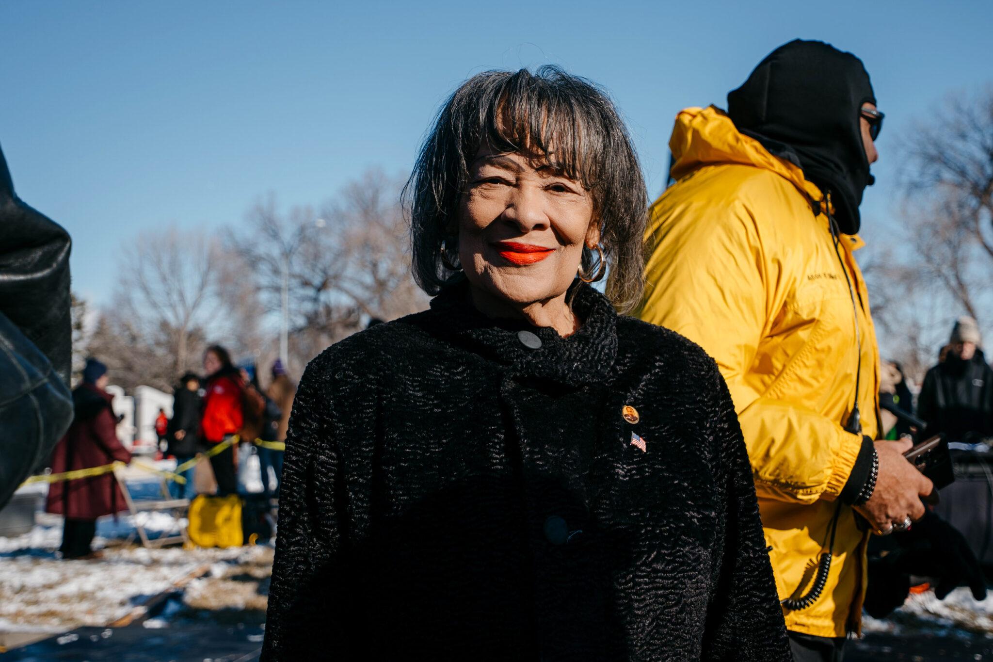 A woman in a black sweater smiles at the camera with red-tinted lips.