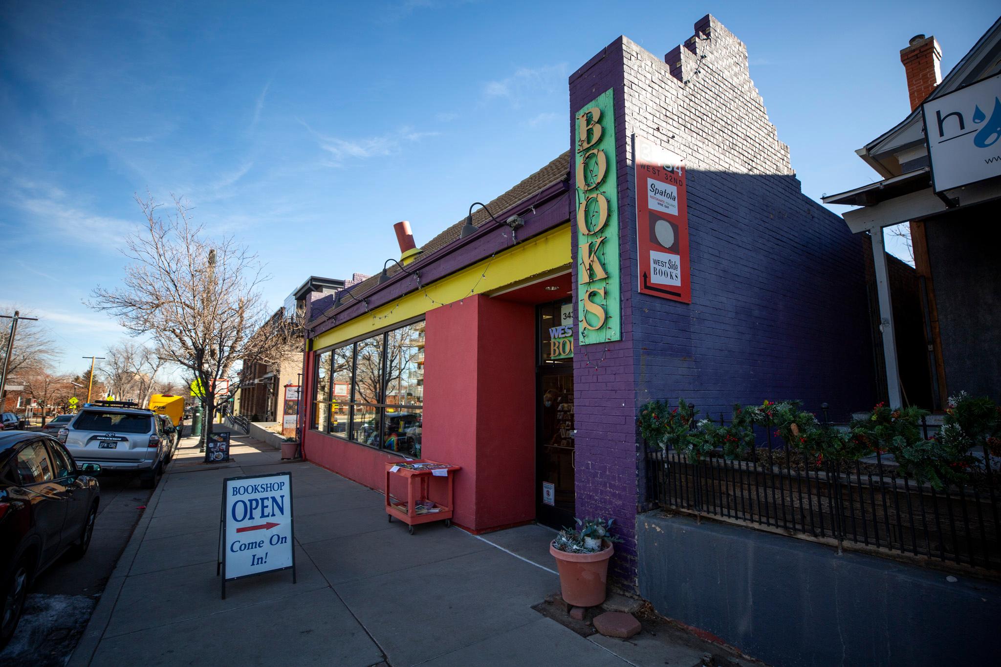 A building of purple, red, yellow and green under a blue sky. A sign by the door reads "BOOKS."