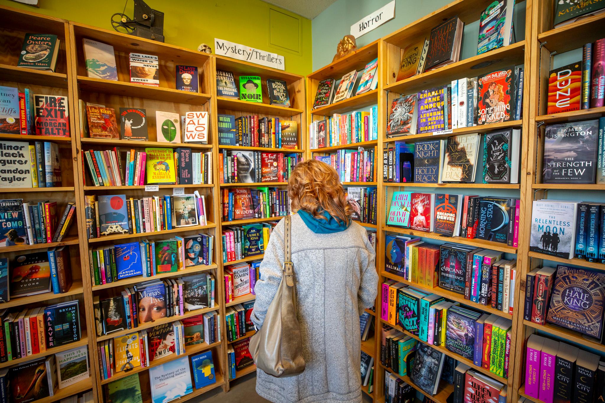 A woman stands in a corner where two rows of bookshelves meet, gazing at the vast, multicolored array of titles.
