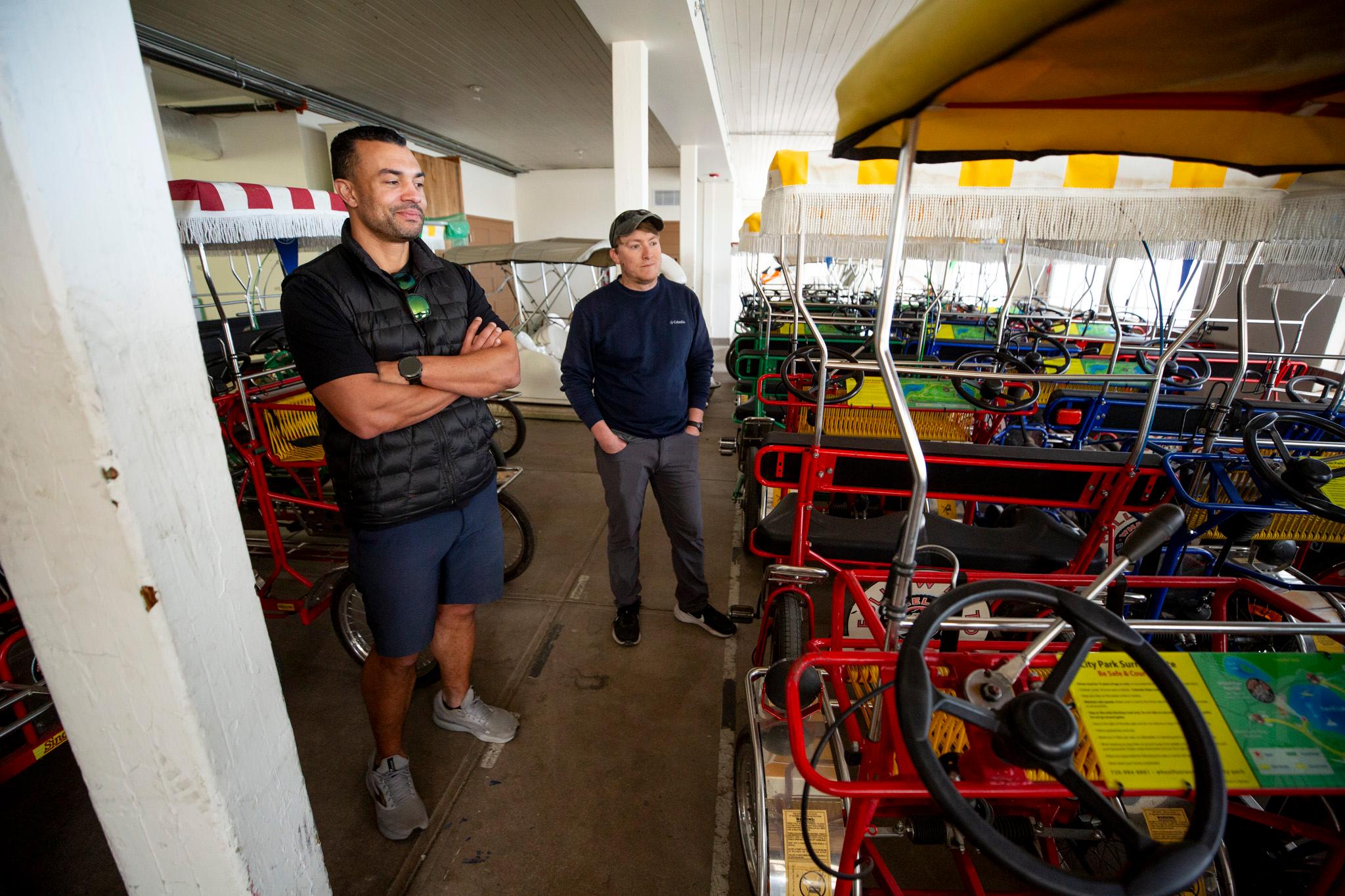 Two men stand in a white room filled with colorful surreys — gold carts with pedals.