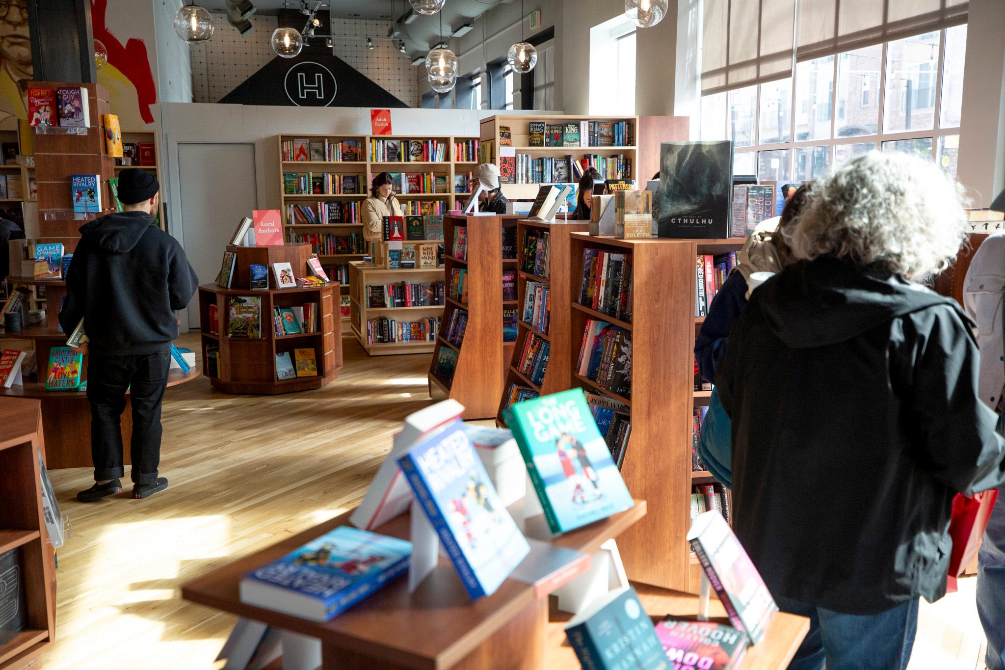 People peruse bookshelves filled with books in a warmly lit room.