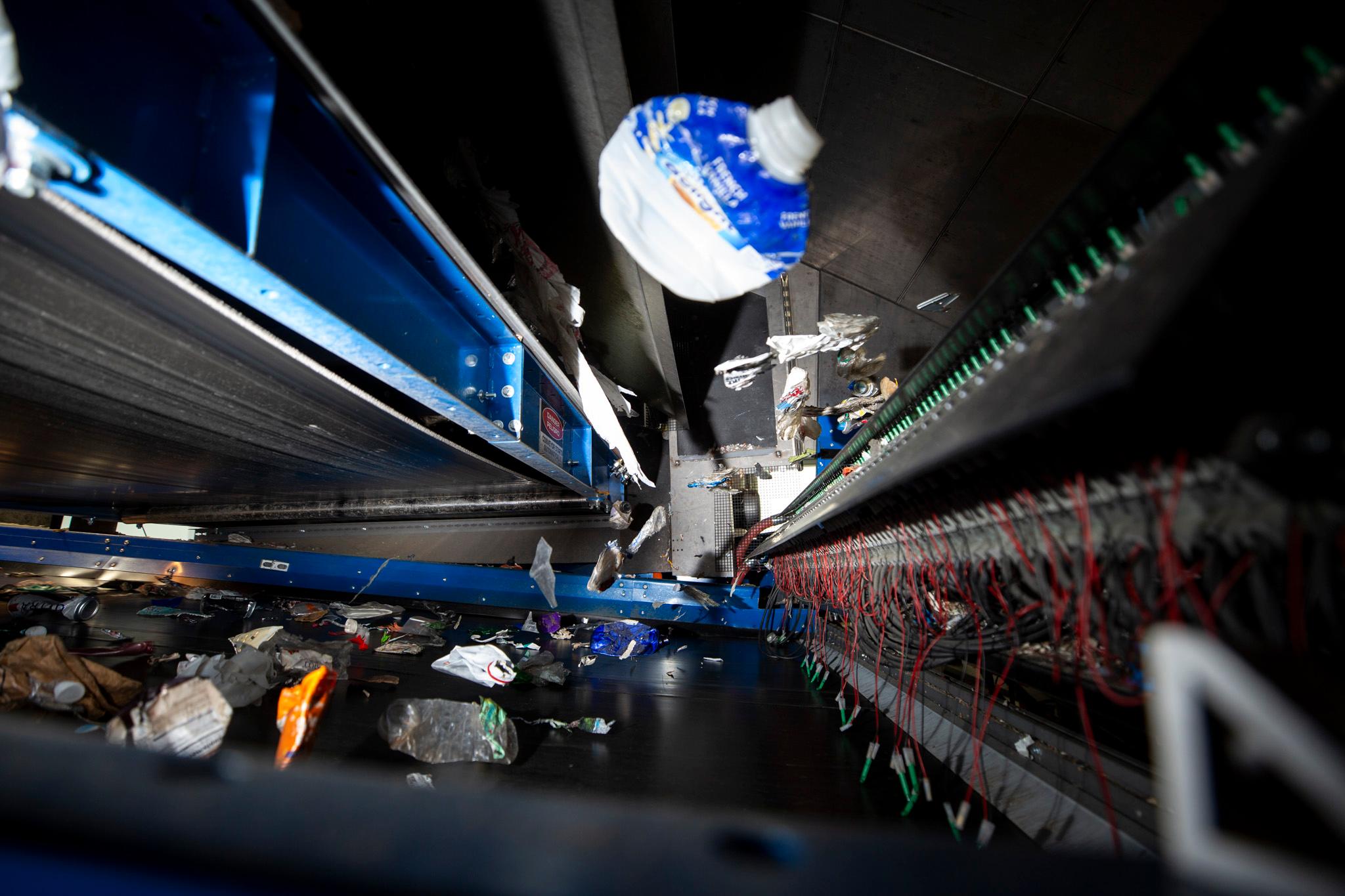 Trash flies through the air inside a puzzle of black and blue conveyor belts.