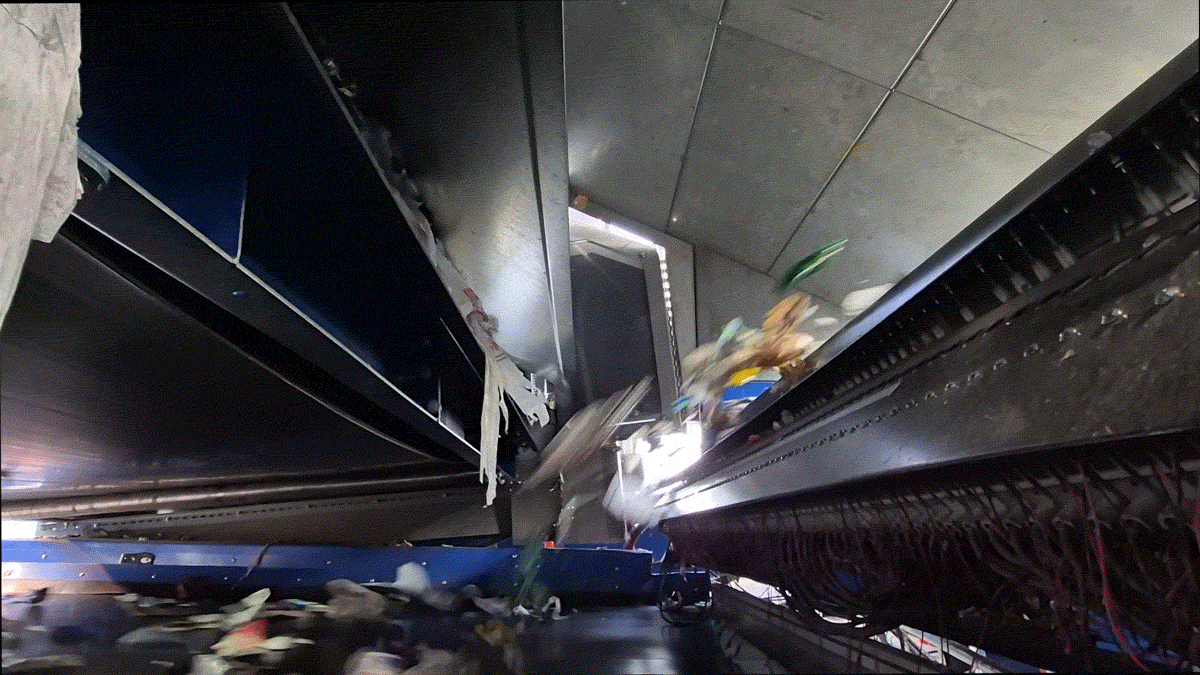 A moving image shows an endless stream of trash flying off of one conveyor belt and onto another: green bottles, brown plastic bags and little bits of white paper.