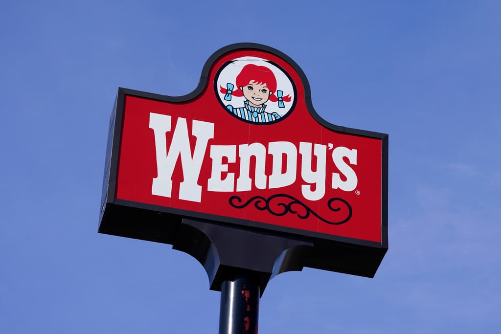 Photographed from below, a red Wendy's sign rises against a cloudless blue sky.