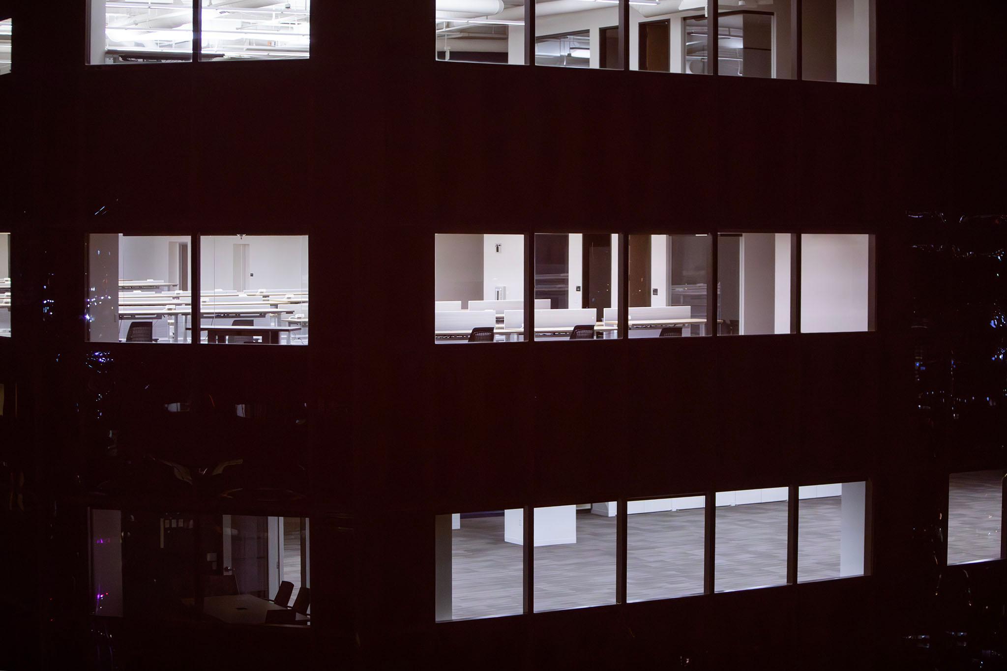 The windows of a dark building glow with white light, showing empty desks and HVAC equipment.