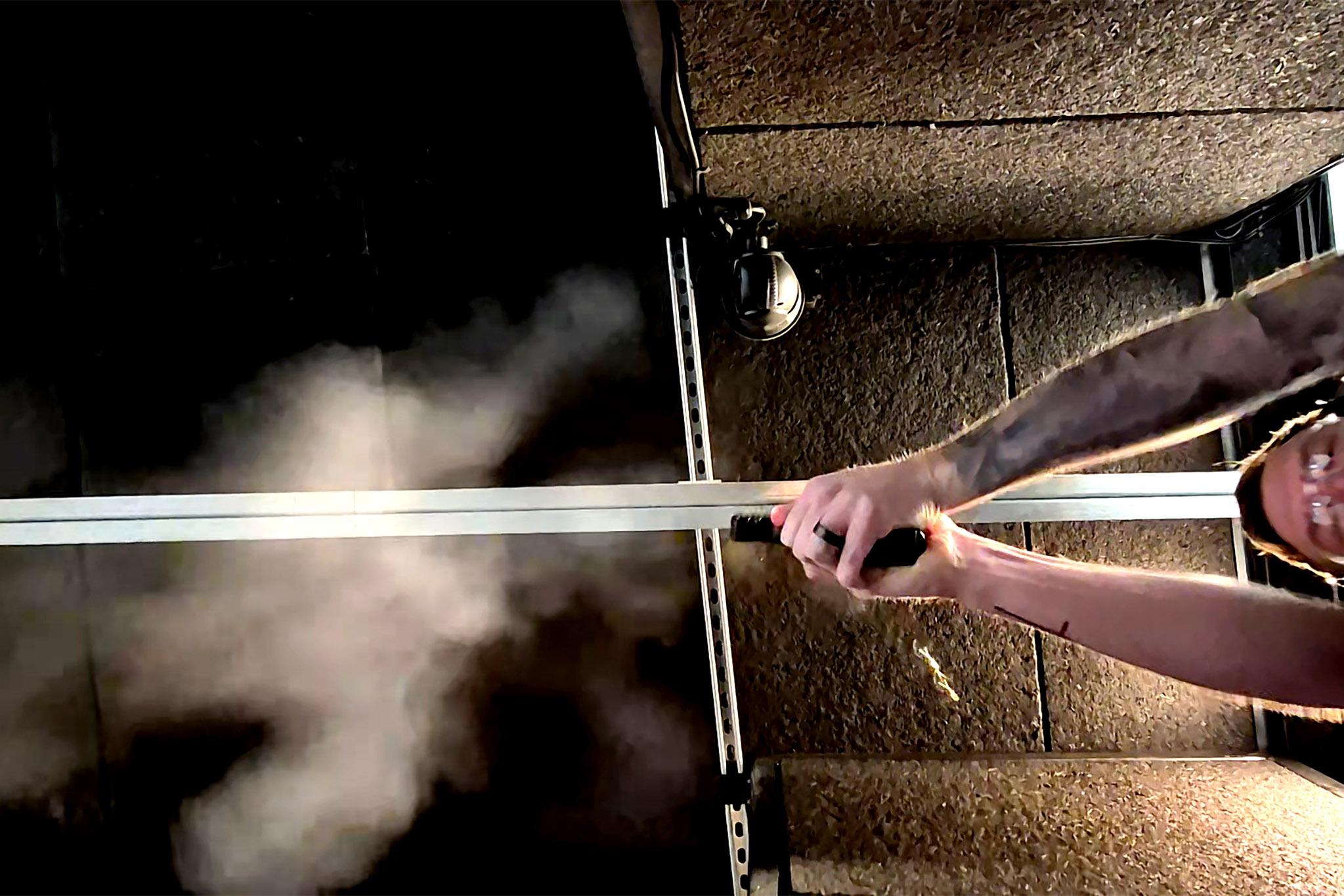 A view up at a man holding a gun. His eyes are closed as a plume of smoke pours out of the barrel.