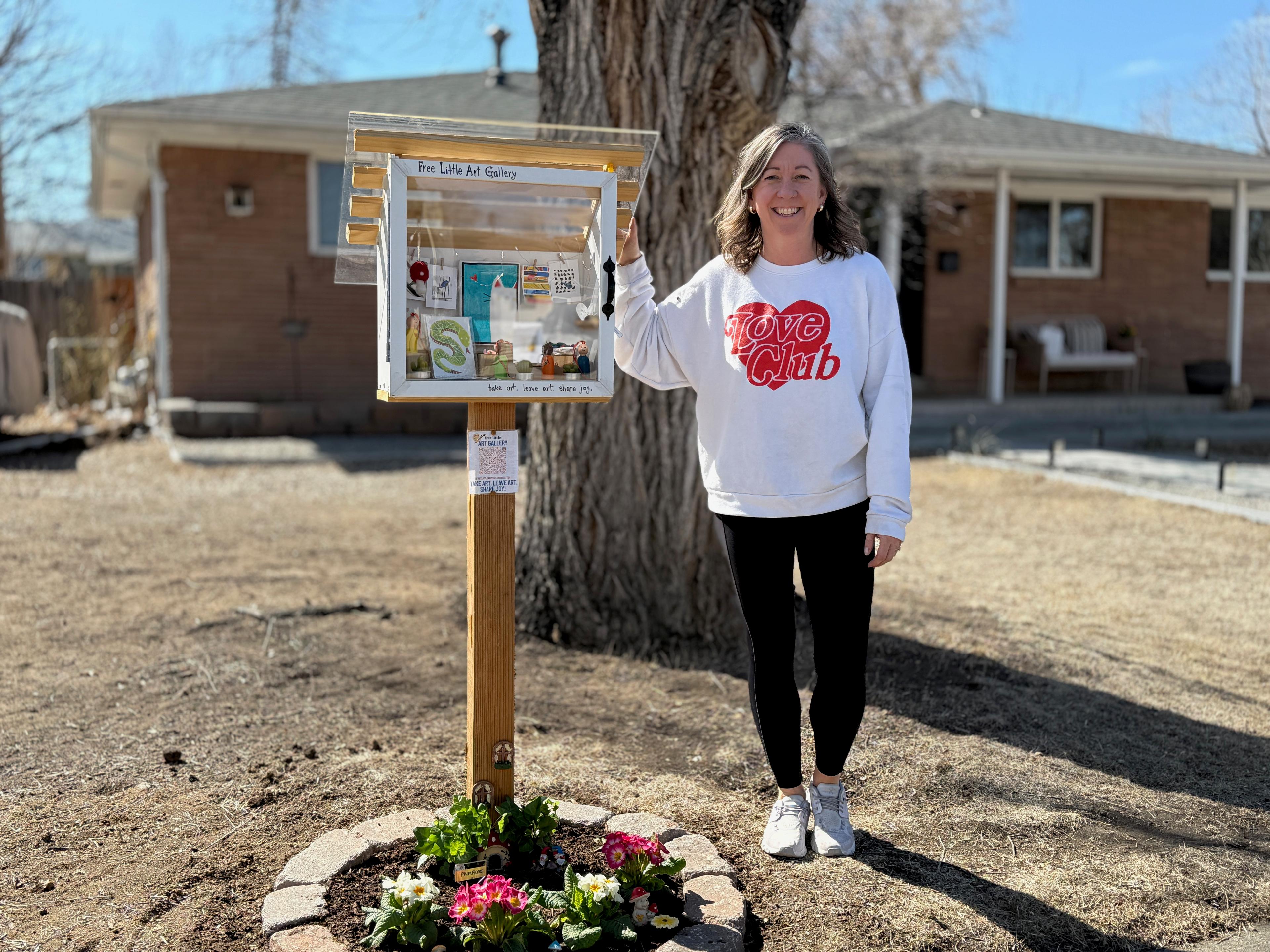 A woman stands and smiles with a small stand filled with art objects.