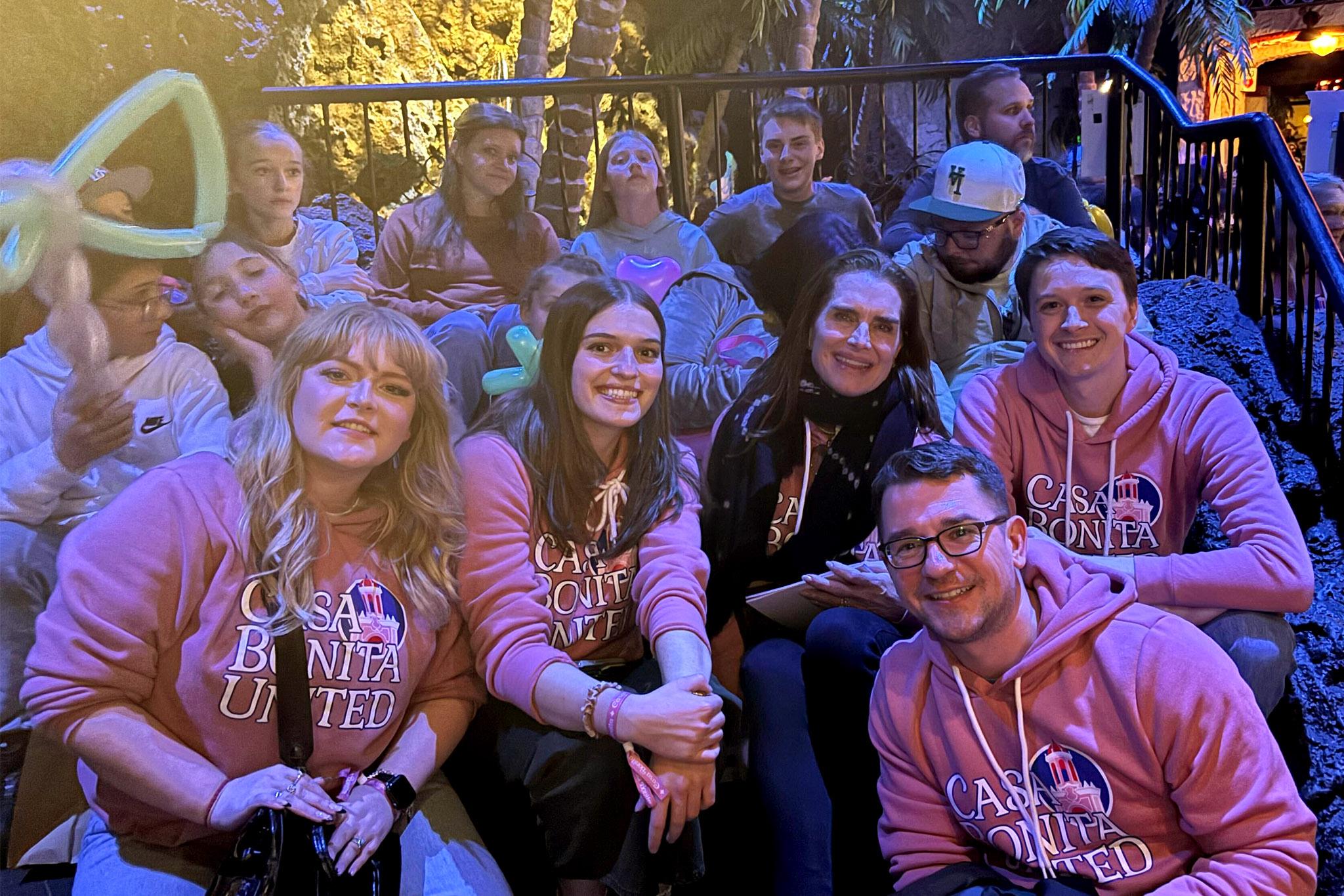 A group of people smile at the camera, many wearing sweatshirts that read "Casa Bonita United."