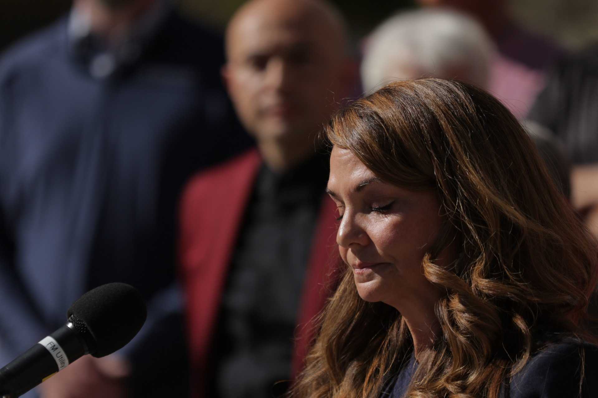 A woman stands in front of a mic, her eyes closed. A group of people stand in the background.