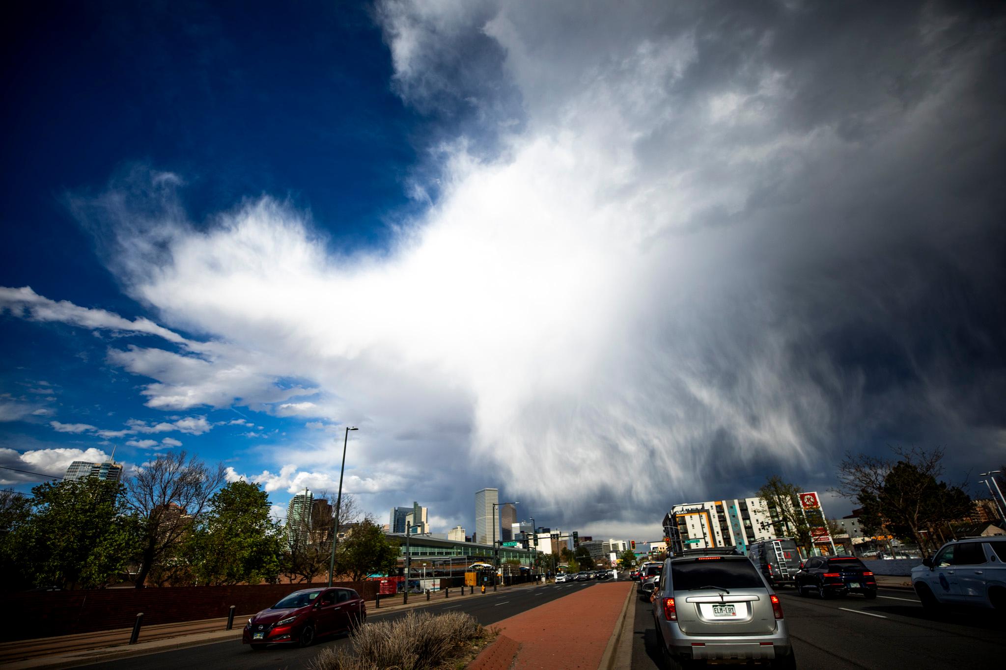Puffy white clouds reach down to a cityscape in an otherwise blue sky, showing tentrils of rain falling in the distance.
