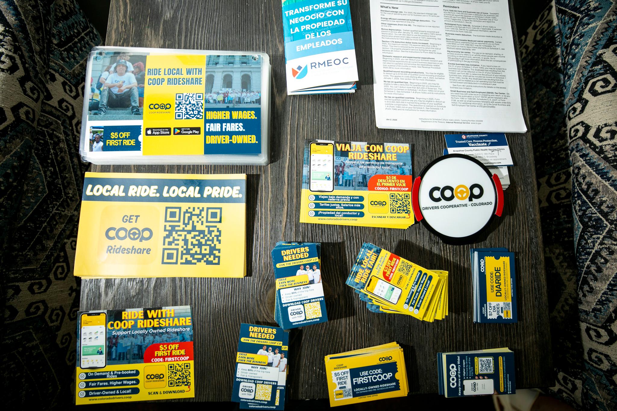 A table with stacks of yellow and blue flyers, postcards and business cards, all showing the Drivers Coop Colorado's logo and info.