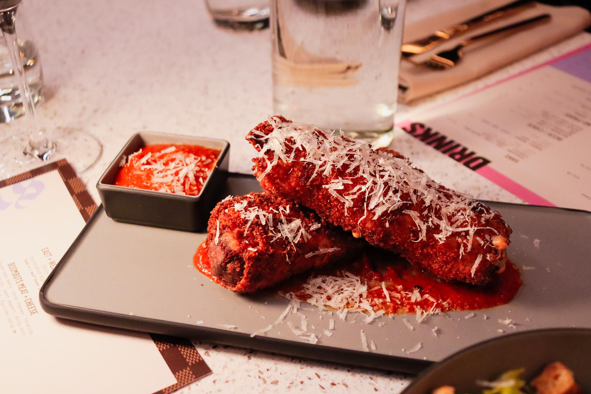 Two giant mozzarella sticks, covered in marinara sauce and cheese, are nestled together on a platter.